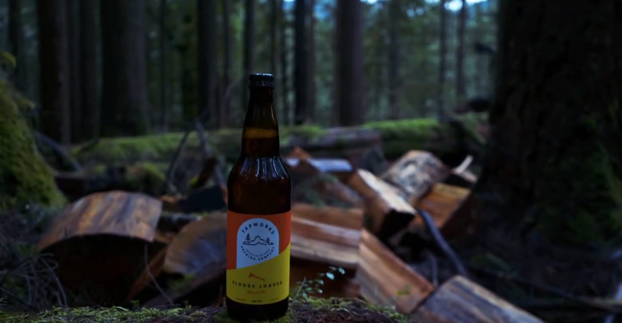 Tapworks Logger beer sitting on a log in the forest.